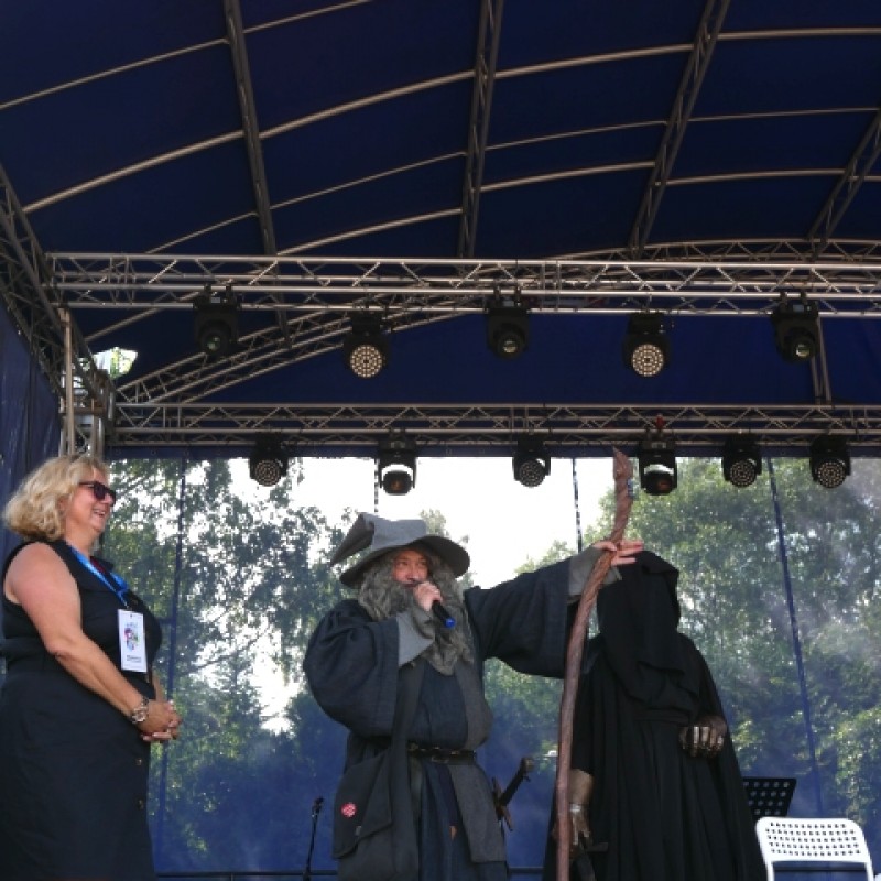 Mężczyzna przebrany za Gandalfa mówi do mikrofonu na scenie, obok niego kobieta i przebrany mężczyzna.