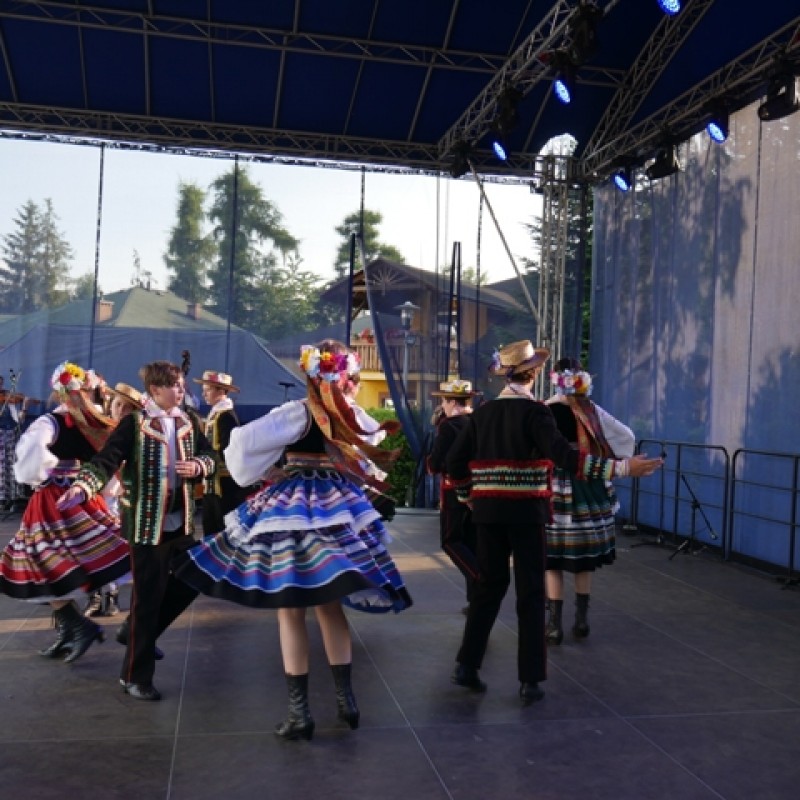Zespół pieśni i tańca w strojach regionalnych na scenie plenerowej.