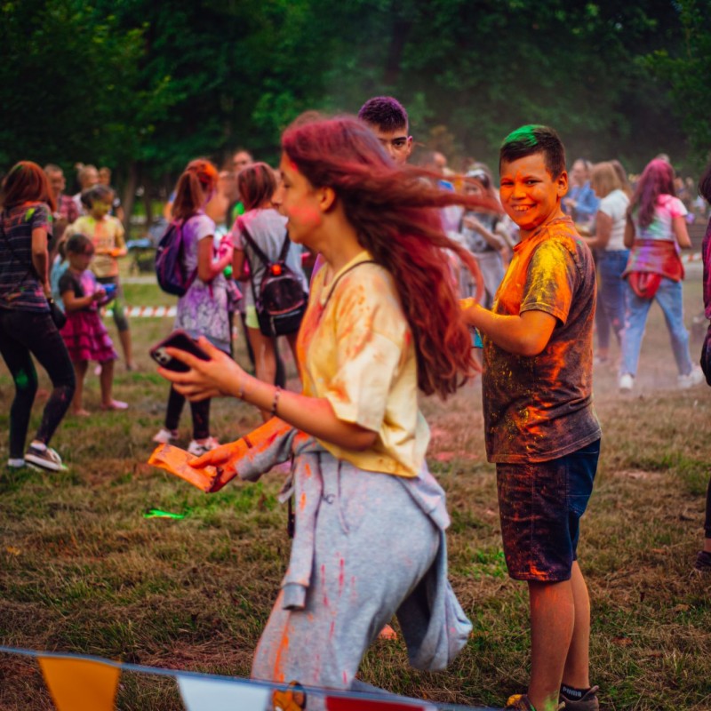 Festiwal kolorów, grupa ludzi ubrudzoną kolorowym proszkiem z uśmiechami na twarzach znajduje się na trawie.