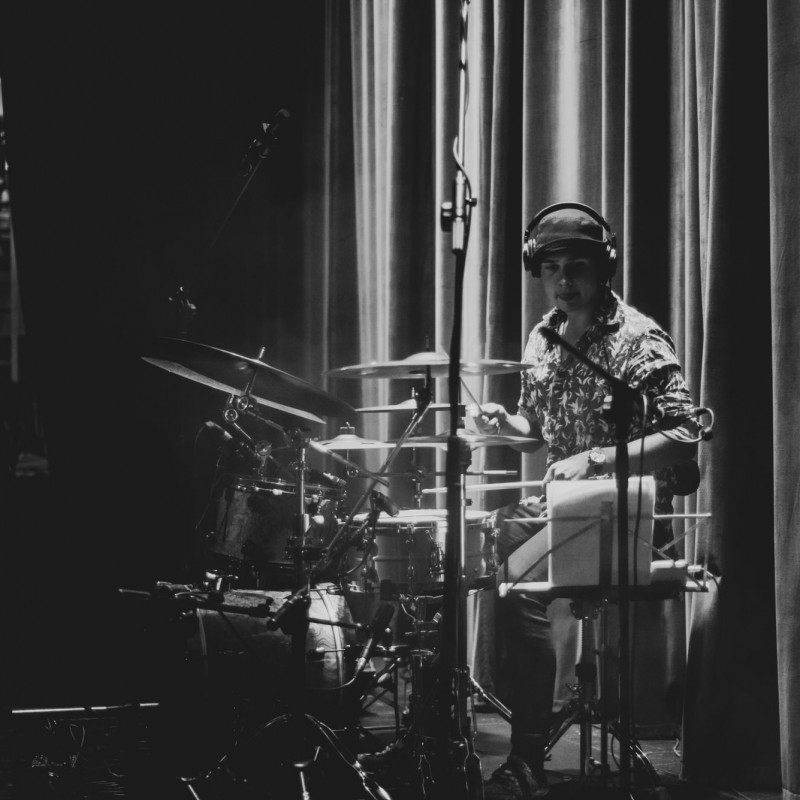 Czarno-białe zdjęcie perkusisty grającego na scenie.