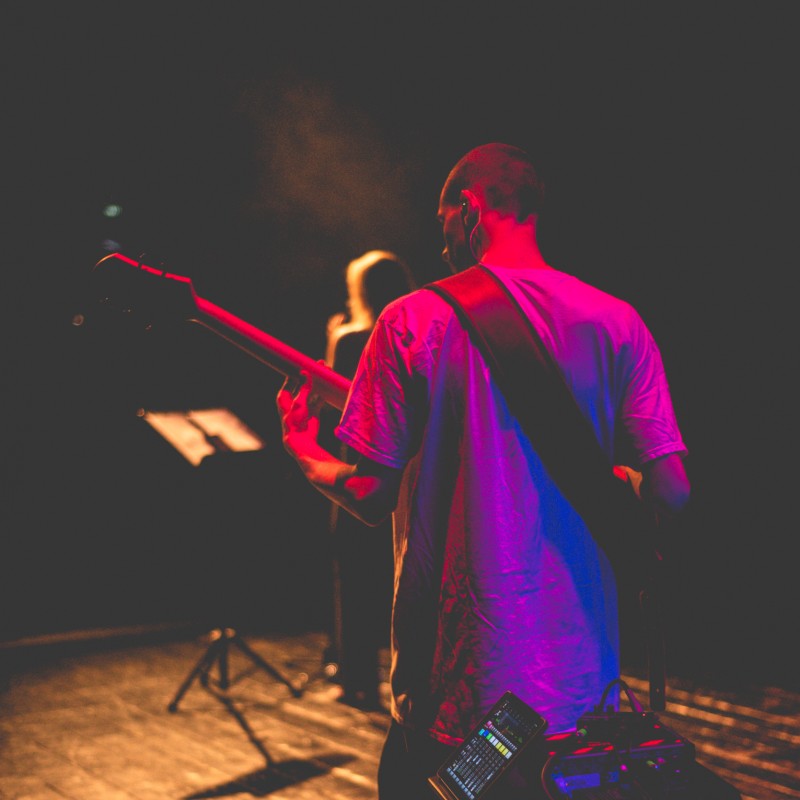 Gitarzysta oświetlony kolorowym reflektorem stoi tyle do obiektywu na sali widowiskowej. 