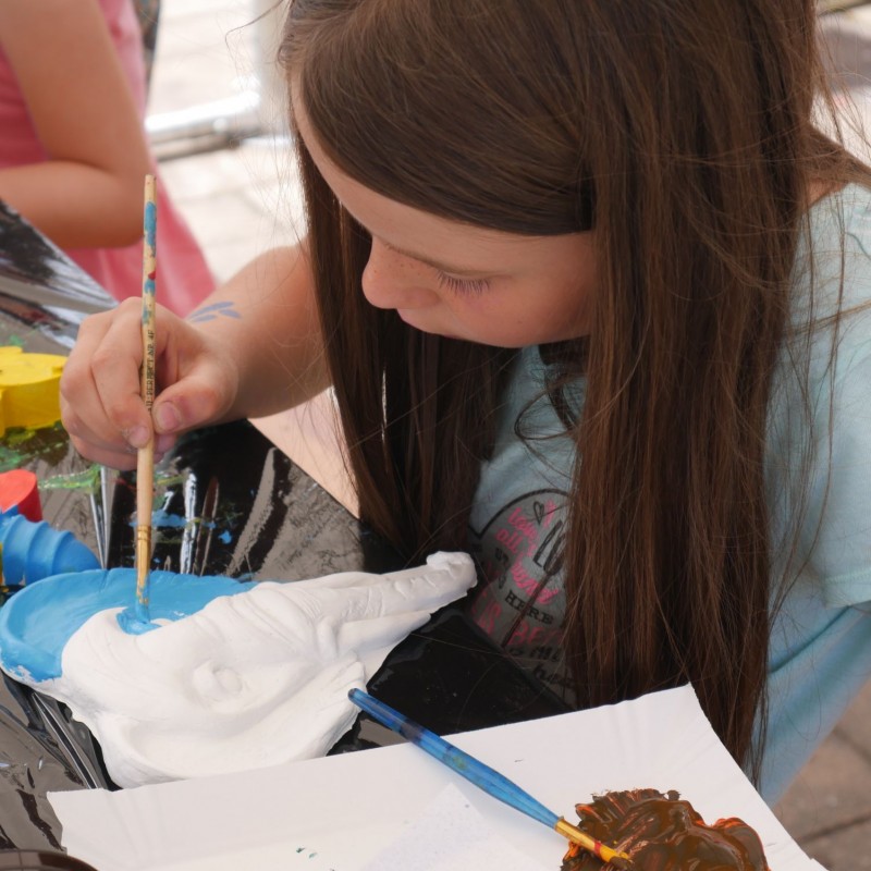 Dziewczynka o długich, brązowych włosach wykonuje malowaną pracę plastyczną.