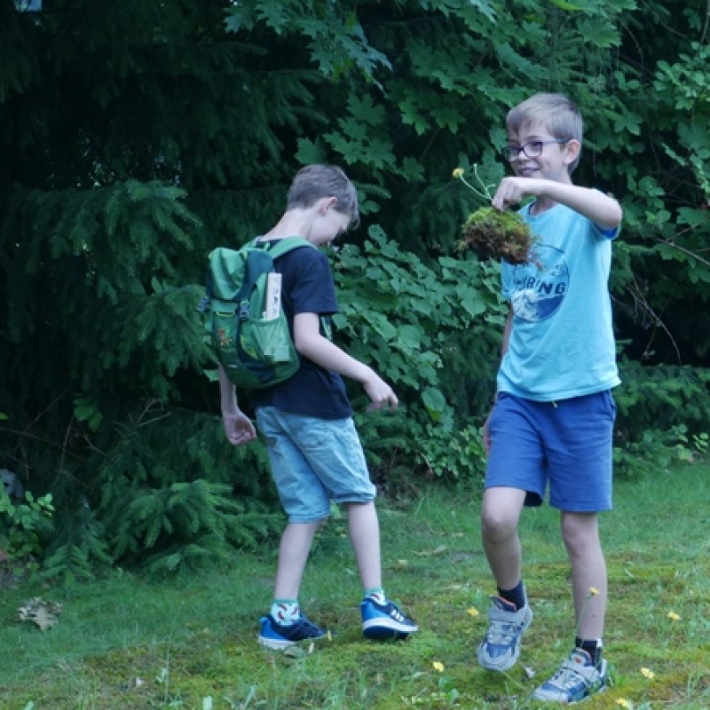 Dwóch chłopców w ruchu, jedne z nich trzyma kępkę ziemi z kwiatami.