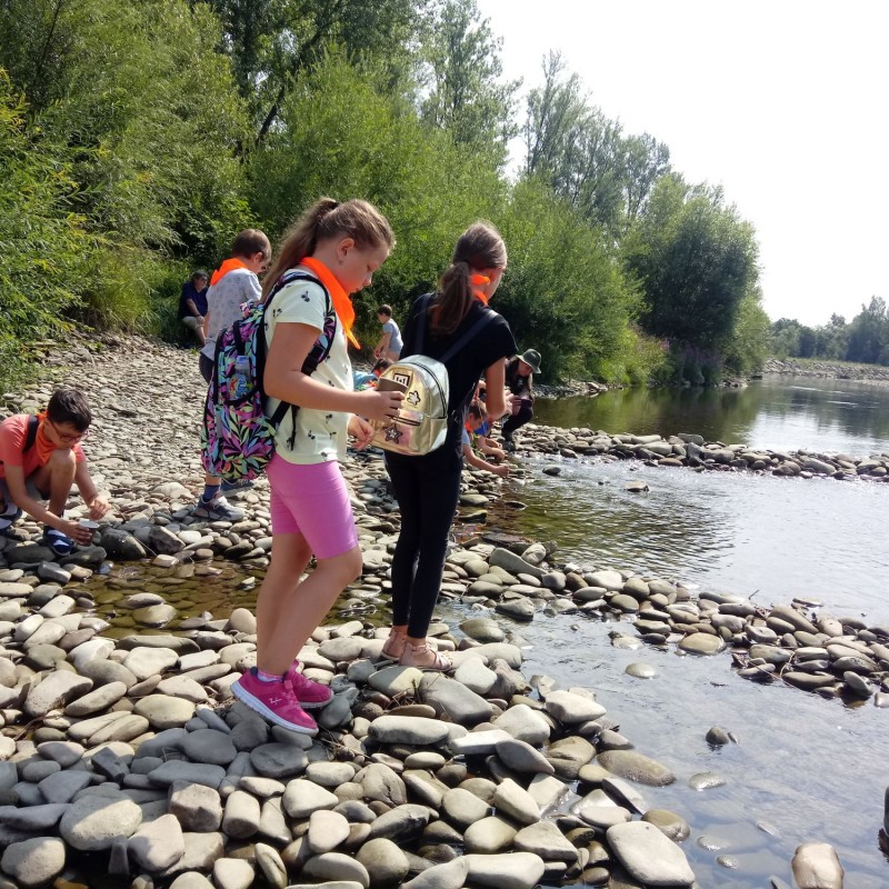 Dzieci stoją nad brzegiem rzeki i patrzą w taflę wody.
