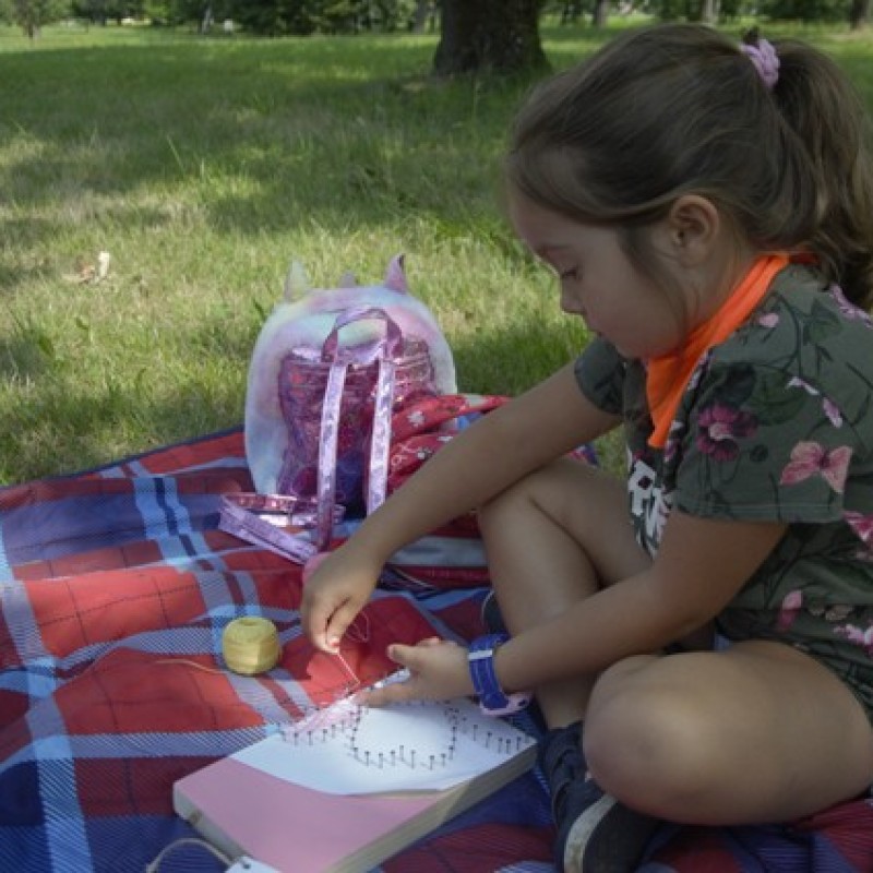 Dziewczynka siedzi na kocu i dekoruje książkę.