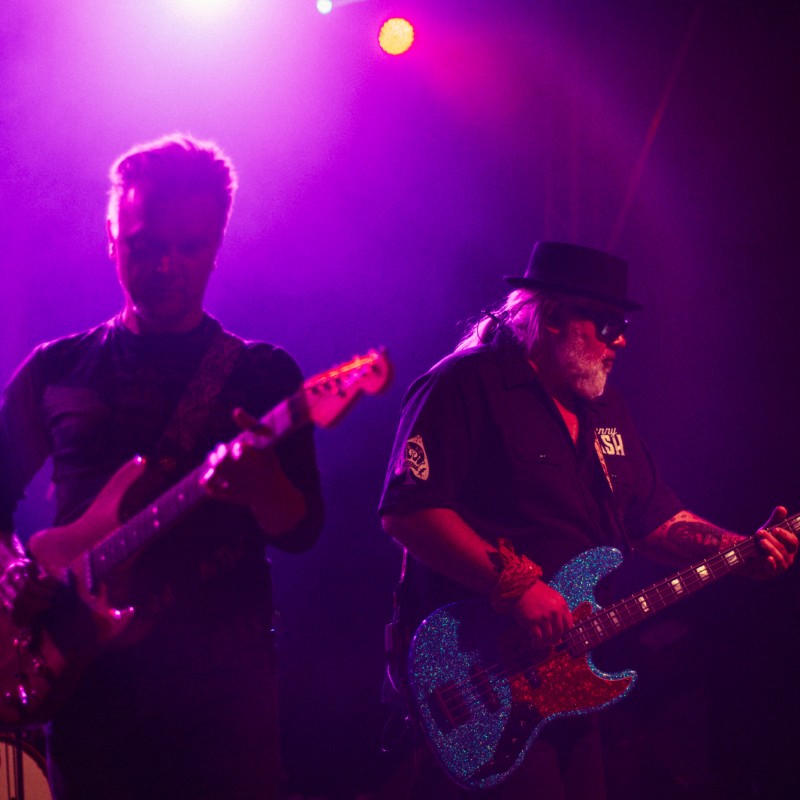 Gitarzyści w świetle fioletowych reflektorów podczas występu.