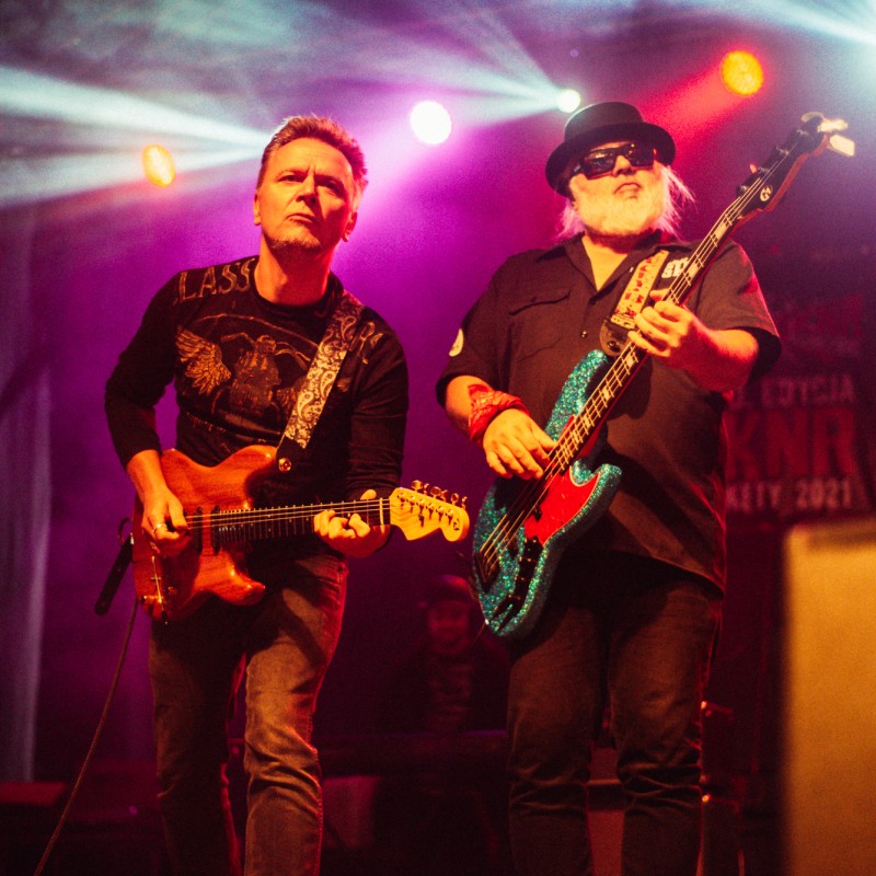 Dwóch gitarzystów na scenie w świetle kolorowych reflektorów.