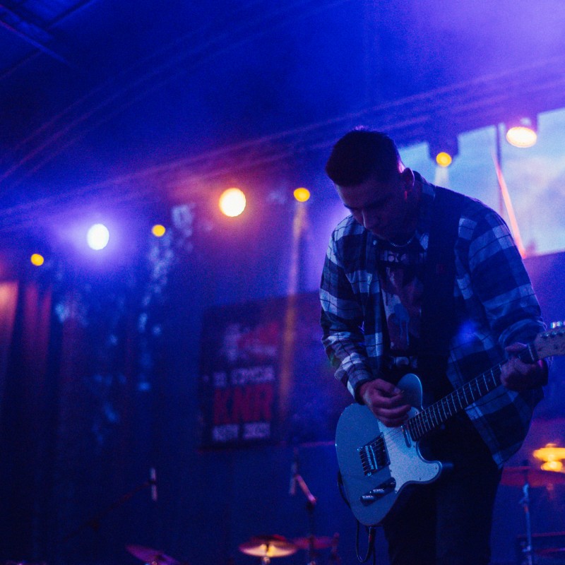 Gitarzysta podczas występu na scenie w przygaszonym świetle reflektorów.