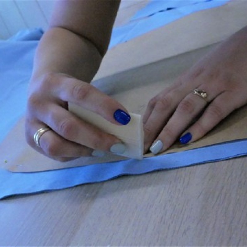 Kobiece dłonie z niebiesko-białymi paznokciami, obrysowują szablon na niebieskim materiale, za pomocą krawieckiego mydła.