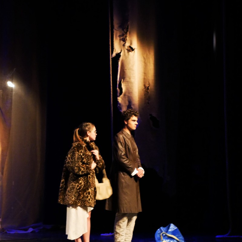 Na scenie kobieta z mężczyzną w płaszczach. Obok, na scenie niebieska reklamówka. 