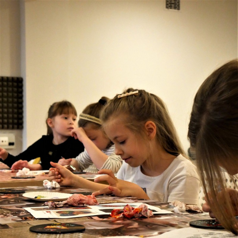 Na zdjęciu dziewczynki, które w skupieniu przy wykorzystaniu palców tworzą dzieło z kropek. 
