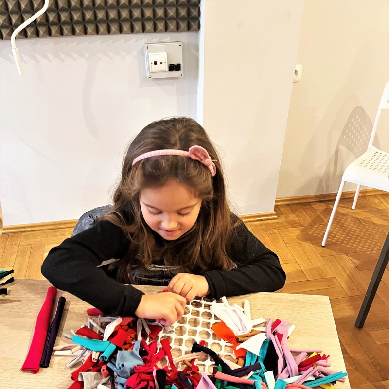 Dziewczynka siedzi przy stoliku i tworzy plastyczny projekt z materiału.