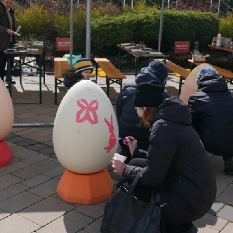 Ludzie malujący ogromnej wielkości jajka wielkanocne różowymi farbami.