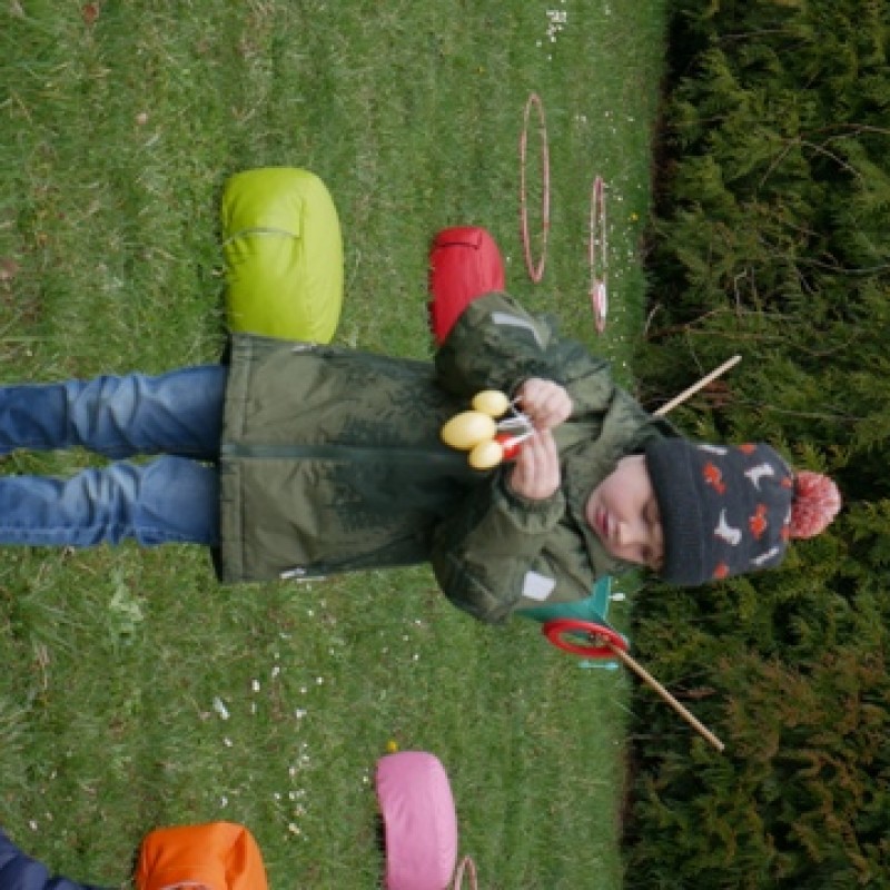 Mały chłopczyk na trawie przed domem kultury trzymający w dłoniach małe jajka wielkanocne.
