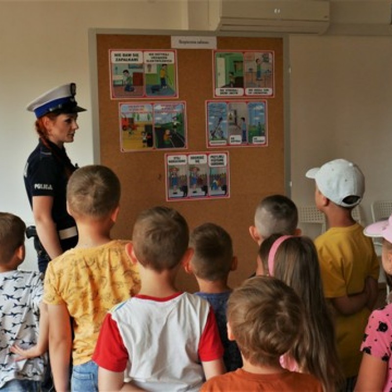 Pani policjantka pokazuje na tablicy korkowej grafiki grupie dzieci.