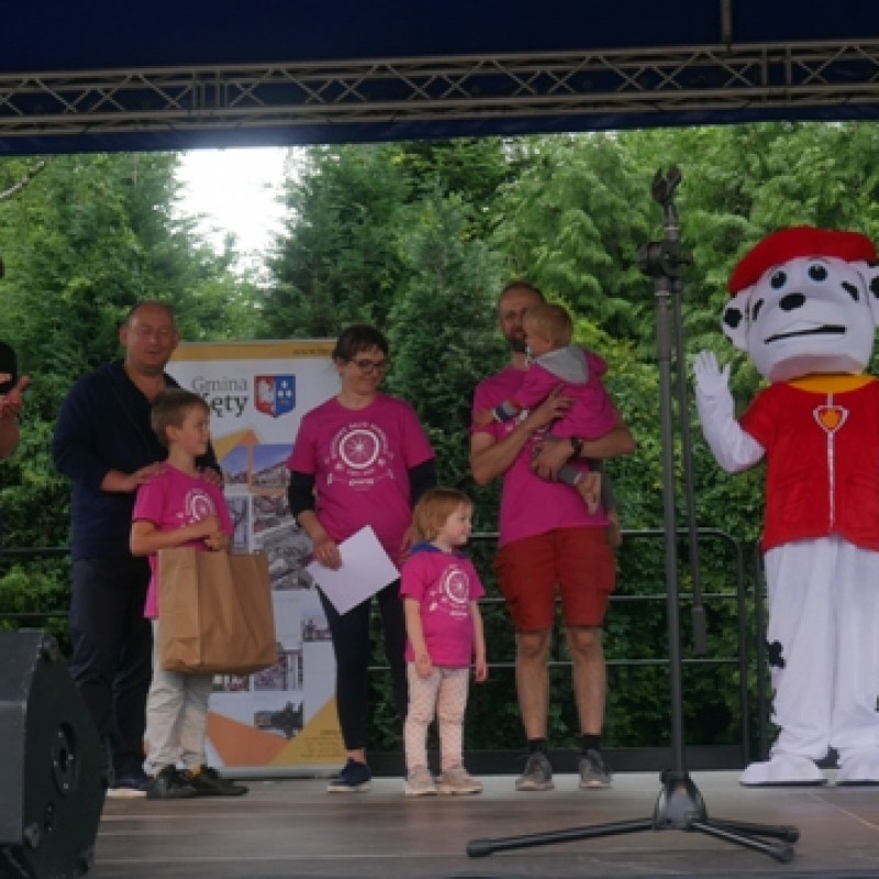 Rozdanie nagród po rajdzie, na scenie osoba przebrana za psa, wicedyrektor domu kultury, burmistrz gminy Kęty oraz rodzina w różowych koszulkach otrzymująca nagrody.
