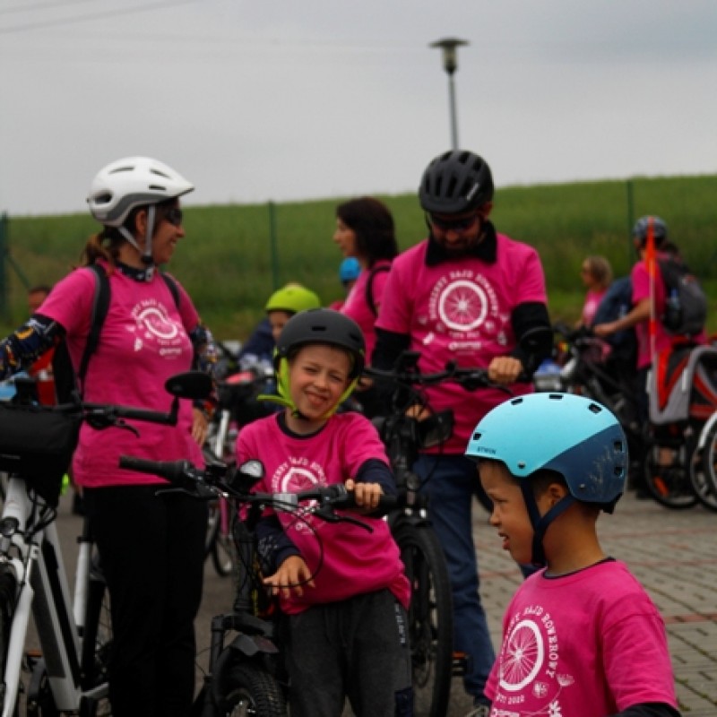 Rodzina na postoju podczas rajdu rowerowego w różowych koszulkach. W tle inni uczestnicy wycieczki.