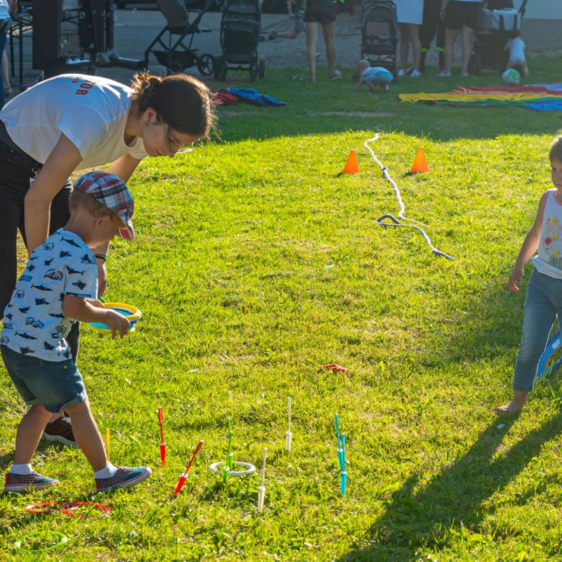Fot. Łukasz Kuc/Dwójka małych dzieci gra w grę z kolorowymi krążkami na trawie w obecności pani opiekunki w słoneczny dzień.