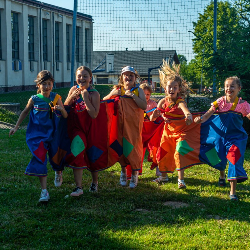 Fot. Łukasz Kuc/Szóstka uśmiechniętych dzieci biegnie na trawie ubrana w dwie pary potrójnych spodni.
