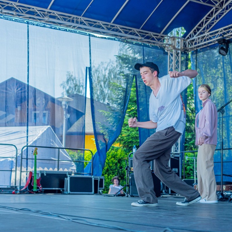 Fot. Łukasz Kuc/Kilkunastoletni chłopiec tańczy na scenie plenerowej domu kultury, z tyłu przygląda się mu dziewczyna.
