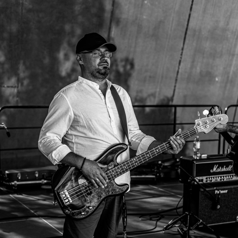 Fot. Łukasz Kuc/Czarno-białe zdjęcie, mężczyzna gra na gitarze basowej na scenie.