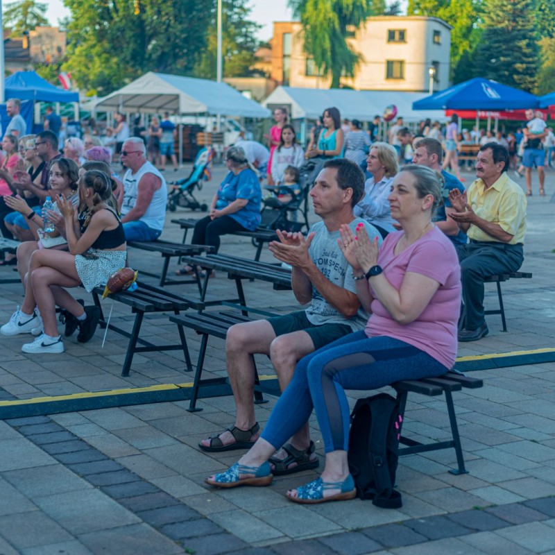 Fot. Łukasz Kuc/Ludzie klaszczą siedząc na placu przed sceną na ławeczkach ustawo nich w rzędach.