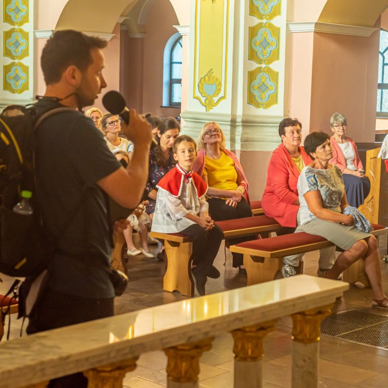 Fot. Łukasz Kuc/Mężczyzna z plecakiem mówi do mikrofonu w kościele, na ławeczkach siedzą ludzie przysłuchując się.