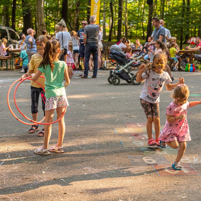 Fot. Łukasz Kuc/Dzieci bawiące się na placu w lesie, dwójka gra w klasy a pozostali trzymają hula hop.