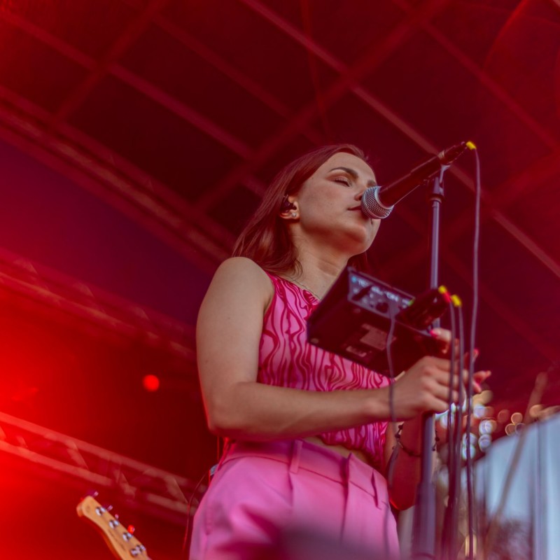 Fot. Łukasz Kuc/Dziewczyna śpiewa do mikrofonu w asyście czerwonych reflektorów na scenie plenerowej.