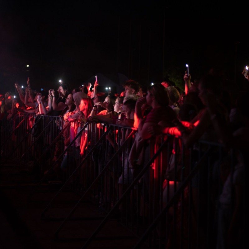 Fot. Łukasz Kuc/Publiczność podczas koncertu wieczorem oświetlona czerwonymi reflektorami z telefonami w dłoniach.