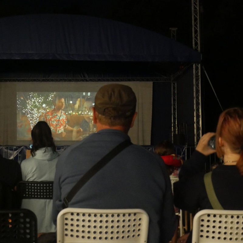 Zbliżenie na plecy pary, która ogląda film w plenerze wyświetlany na dużym ekranie.