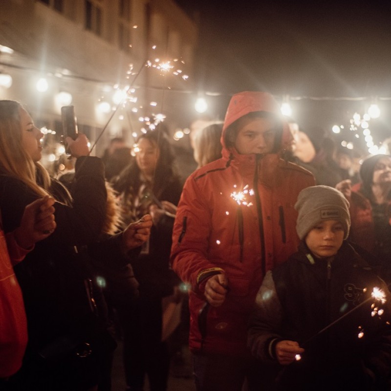 Uczestnicy imprezy swiecący zimne ognie przed fasadą DK Kęty.