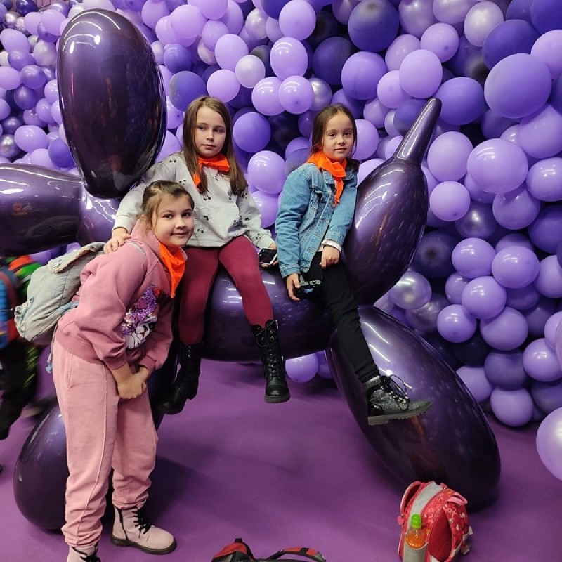 Dzieci siedzące na fioletowych balonach. W tle ściana cała ozdobiona balonami tego samego koloru.