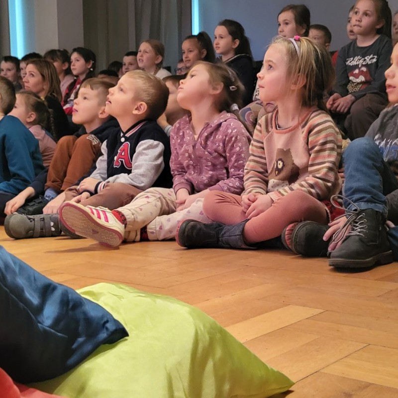 Publiczność w sali studyjnej DK oglądająca występ Filharmonii Krakowskiej. Młodsze dzieci siedzą na kolorowych poduchach, starsze - z tyłu - na krzesłach.